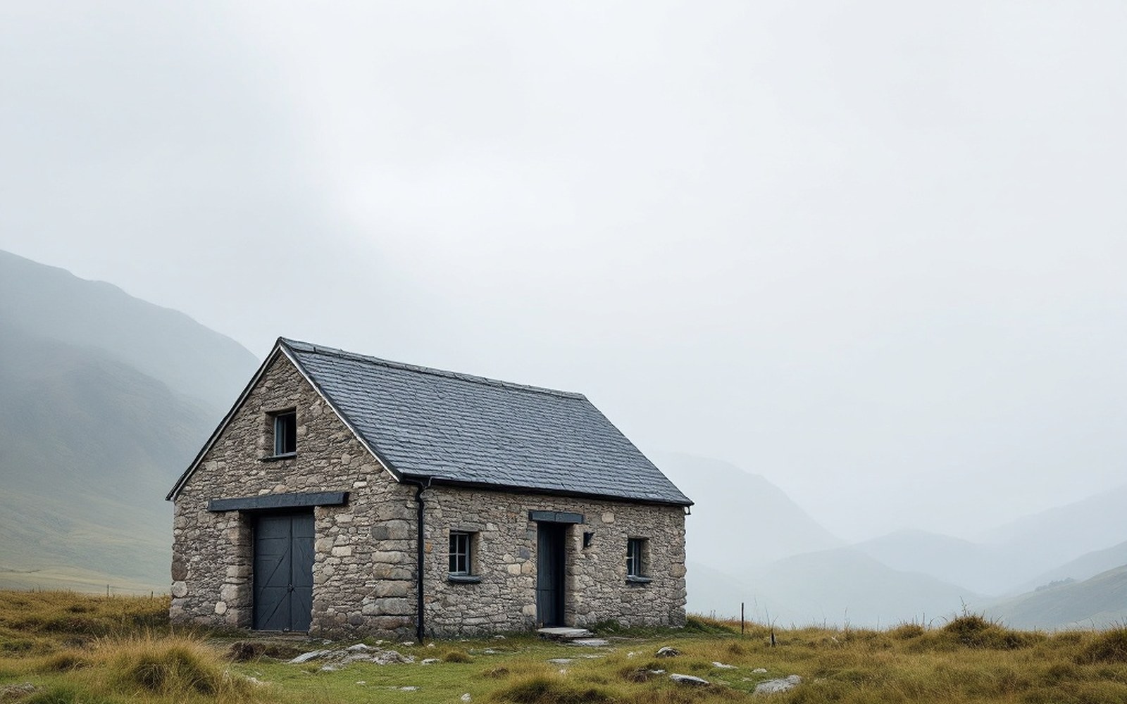 A low stone mountain farm building with a broad slate roof standing alone on high pasture