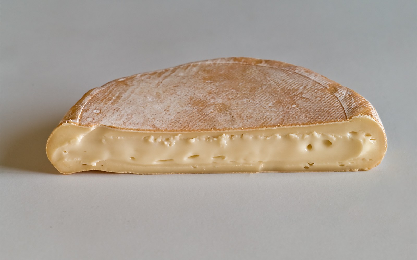 Cross-section of a wedge of reblochon showing its rind and pale, dense interior