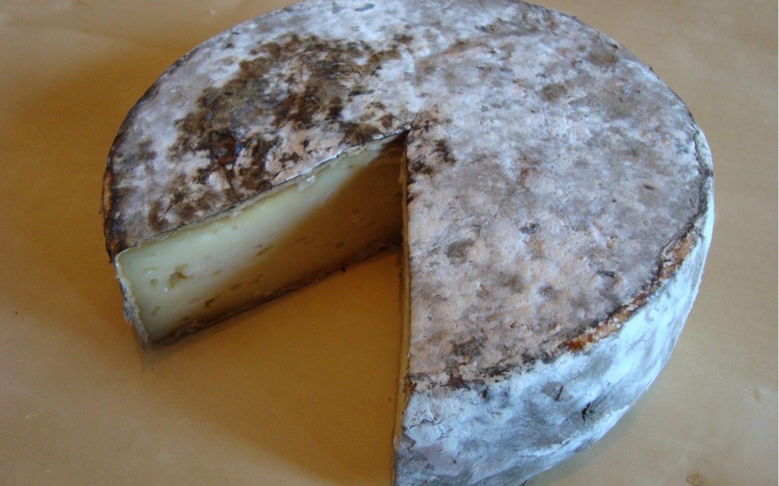 A wheel of Tome des Bauges cheese with a wedge cut out, showing its pale interior